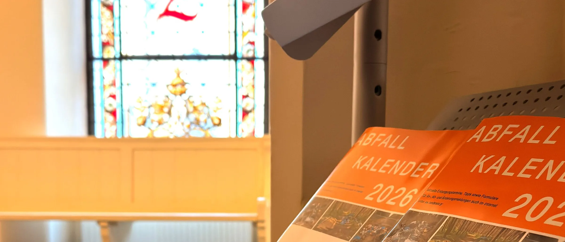 Der Abfallkalender in der Auslage im Rathaus. Im Hintergrund eine Buntglasscheibe des Rathauses