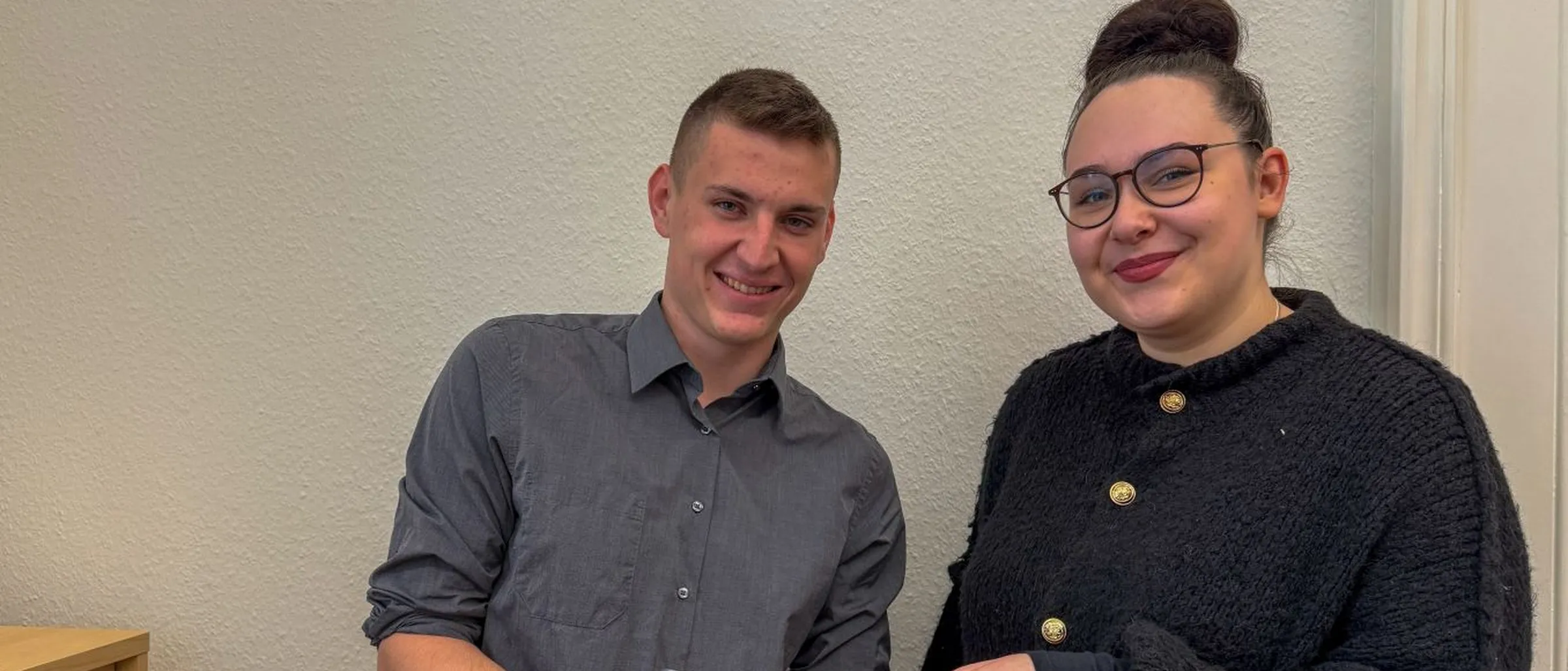 Zwei Auszubildende der Stadtverwaltung halten ein Tablet in der Hand und lächeln in die Kamera