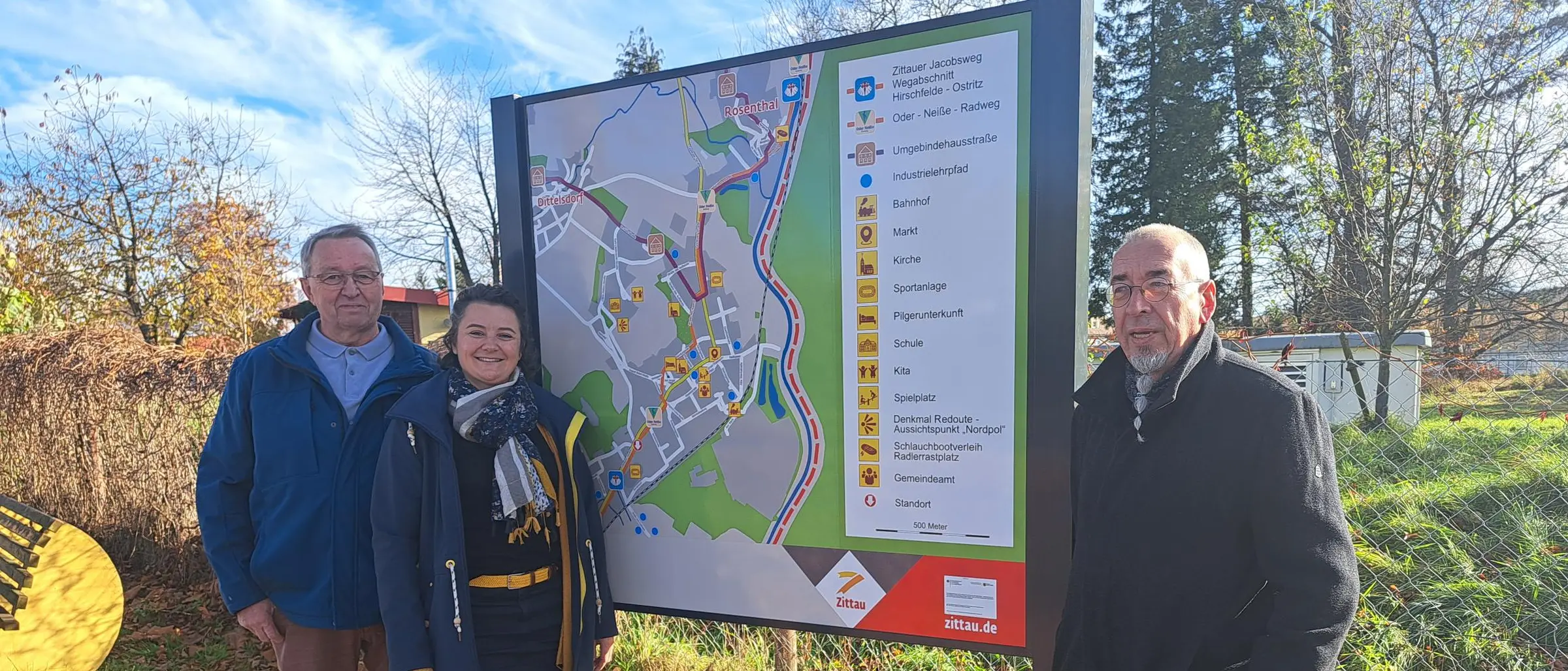 Drei Personen stehen vor einem der neuen touristischen Übersichtsschilder im Ortsteil Hirschfelde.