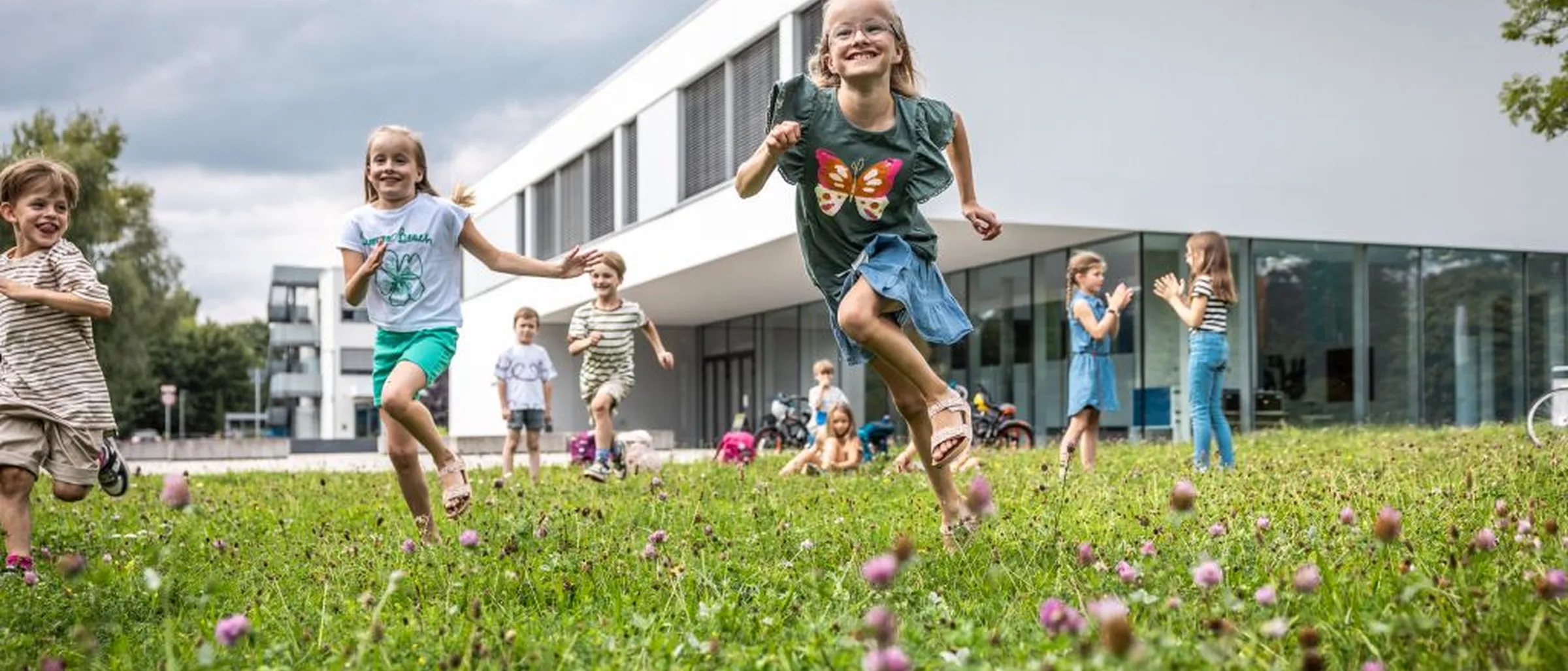 Spielende Kinder auf der Wiese vor einem Hörsaalgebäude der Hochschule