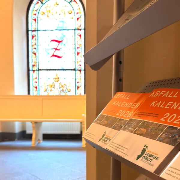 Der Abfallkalender in der Auslage im Rathaus. Im Hintergrund eine Buntglasscheibe des Rathauses