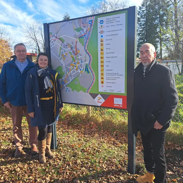 Drei Personen stehen vor einem der neuen touristischen Übersichtsschilder im Ortsteil Hirschfelde.