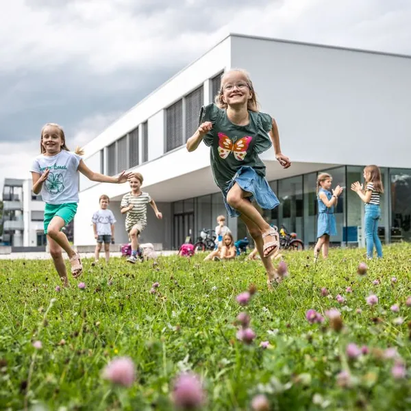 Spielende Kinder auf der Wiese vor einem Hörsaalgebäude der Hochschule